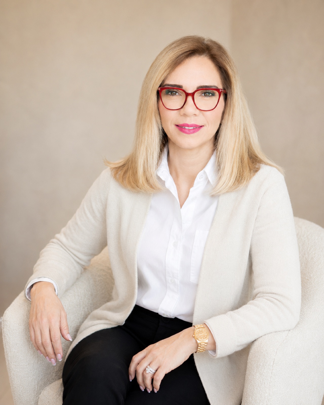 Cream knit cardigan, red frames. Seated, soft ground. Warmest and least tailored.
