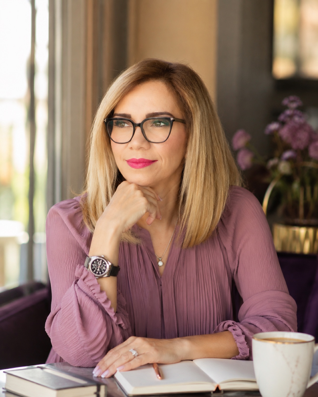 Mauve blouse, black frames. Journal and coffee at a window.