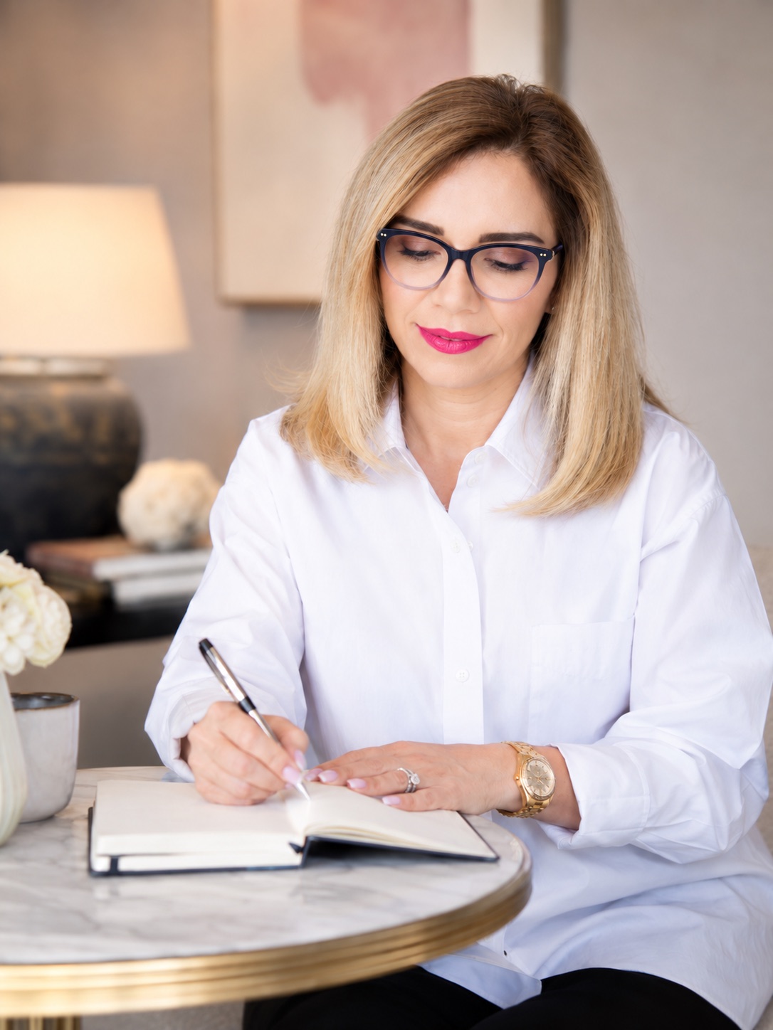 Black frames. Writing in a journal at the round marble table, roses and a lamp behind. Same setup as 69, and the same as 39 in red.