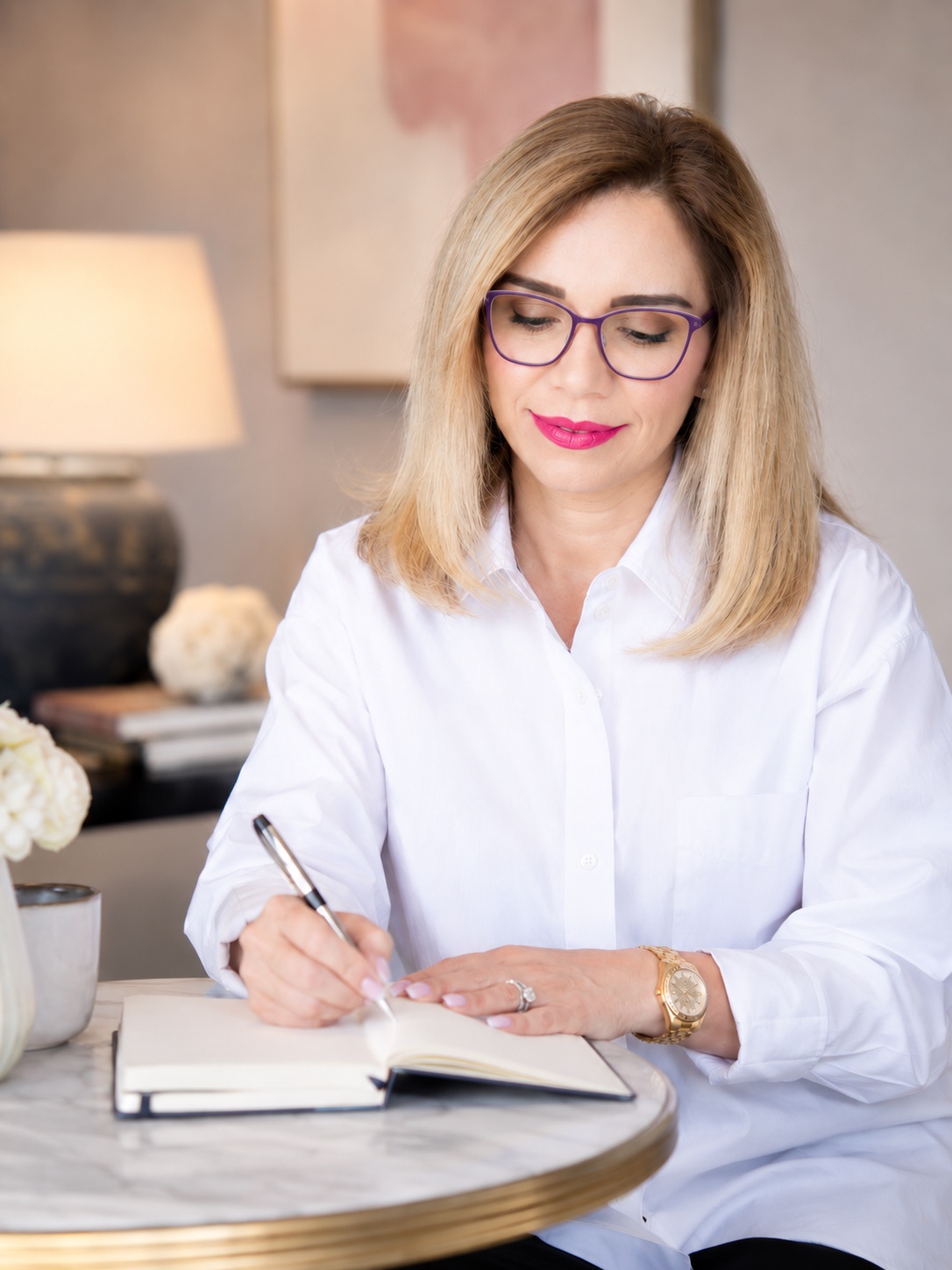 Plum frames. Writing in a journal at the round marble table, roses and a lamp behind. Same setup as 68, and the same as 39 in red.